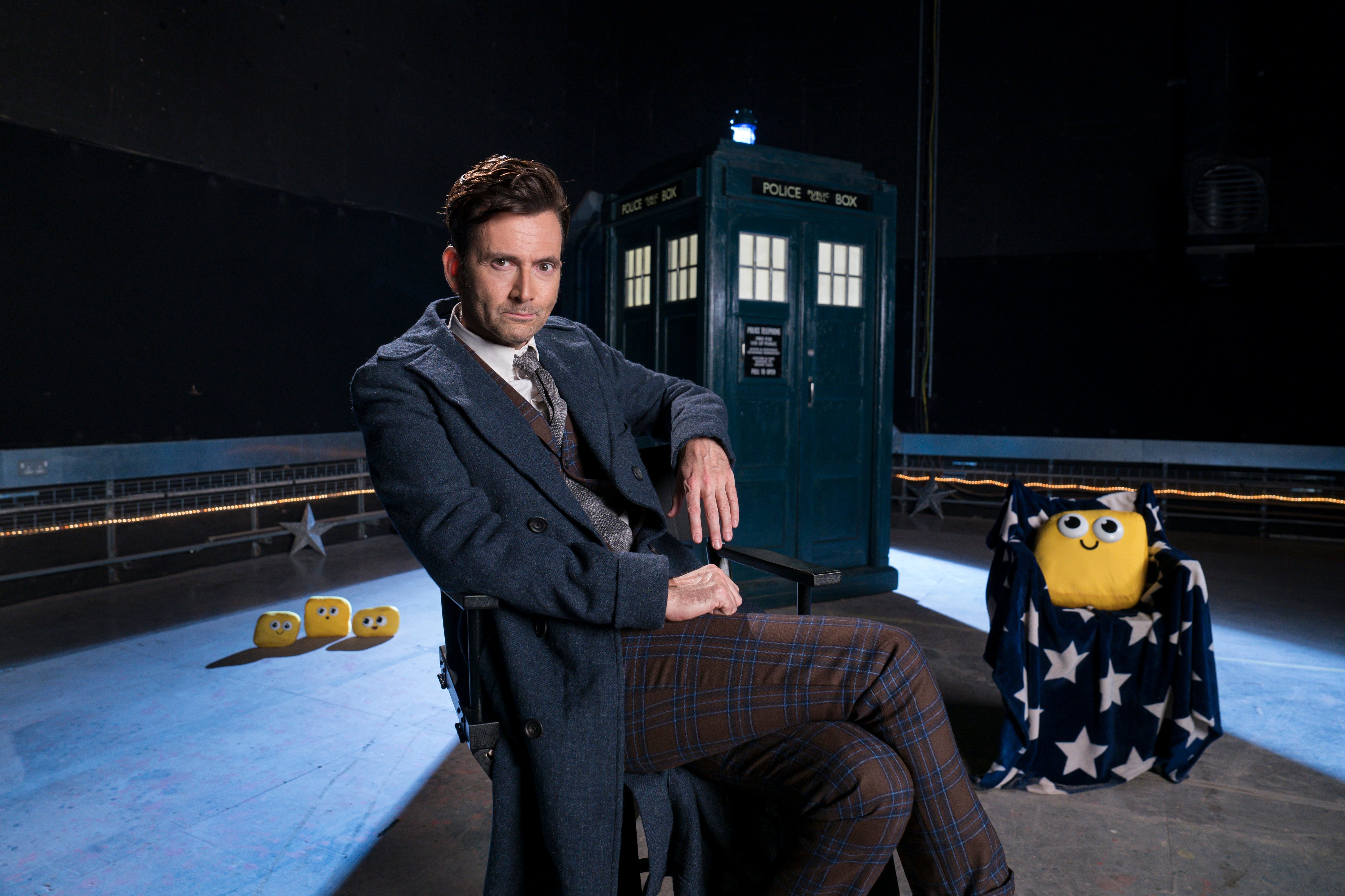The Doctor sits in a chair with Bugbies and his TARDIS behind him.
