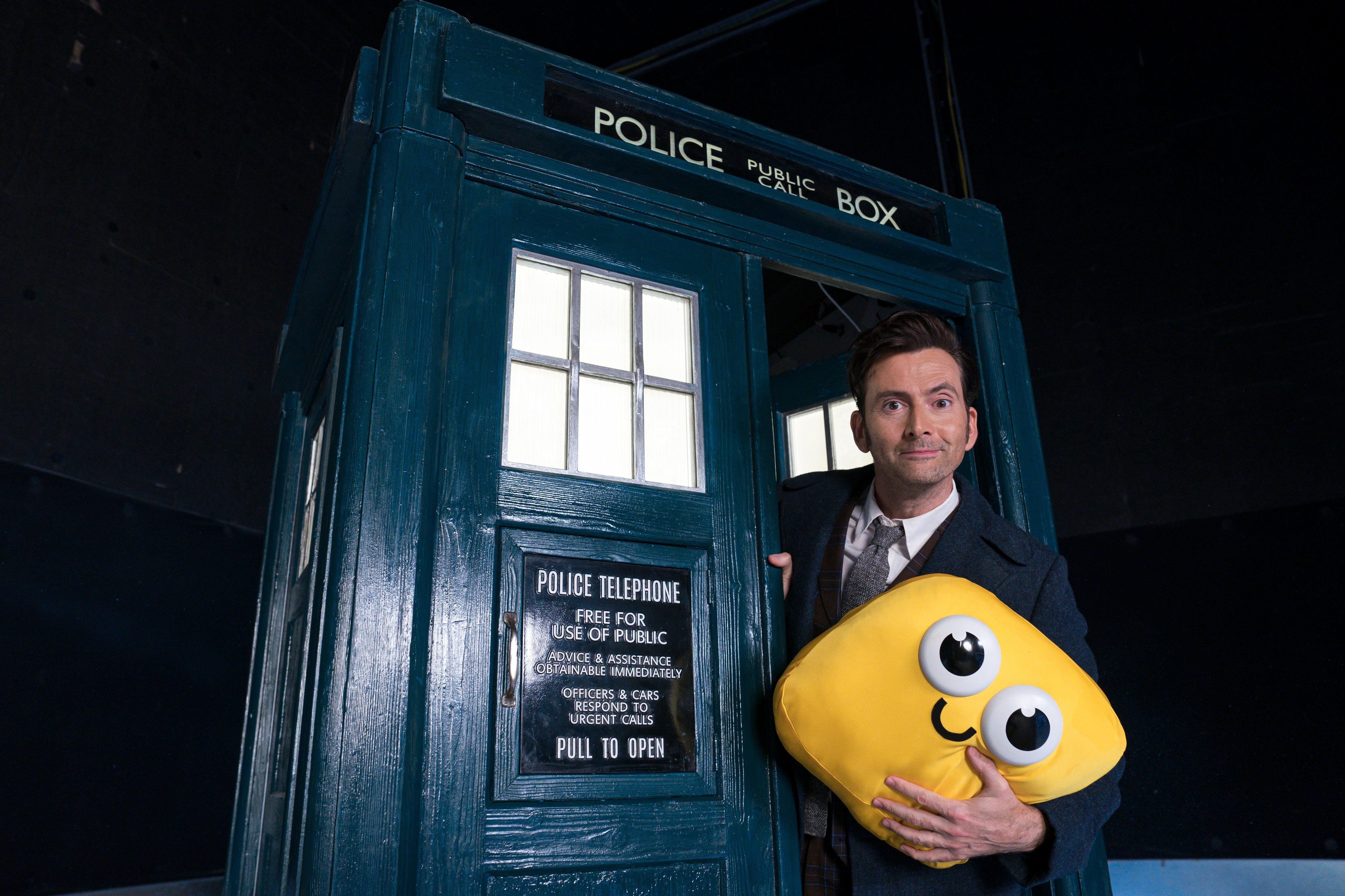 The Fourteenth Doctor, by the doors of his TARDIS, holding a Bigbie.