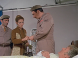 Liz hands the Brigadier a mirror from her purse so that he can help the Doctor see his new appearance.