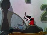 Mickey washes his broom in a bucket of water.