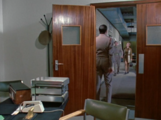 Liz walks down the corridor to Brigadier Alistair Gordon Lethbridge-Stewart's office as he stands ready to greet her.