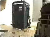 Scott stands outside the Doctor's TARDIS, near a Dalek.